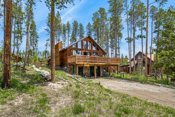 Cluster of rustic log cabins with red metal roofs and decks surrounded by fall foliage and evergreen trees