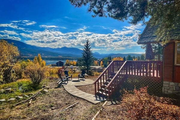 Modern blue house with stone pillars overlooking mountain lake and forested valley with snow-capped peaks