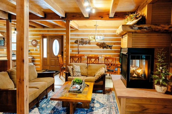 Modern mountain cabin with expansive deck, fire pit seating, grill, and forest views at dusk