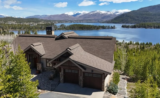 Modern blue and stone mountain home with lake and snow-capped peaks in background